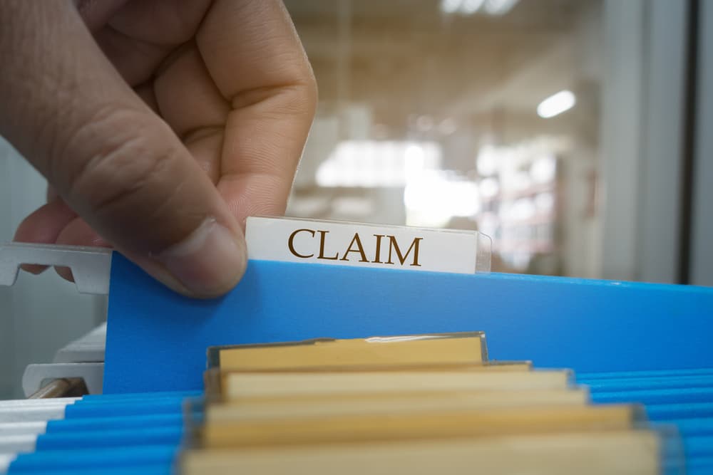 Hand retrieves a claim document from a file for a client, symbolizing the insurance process.