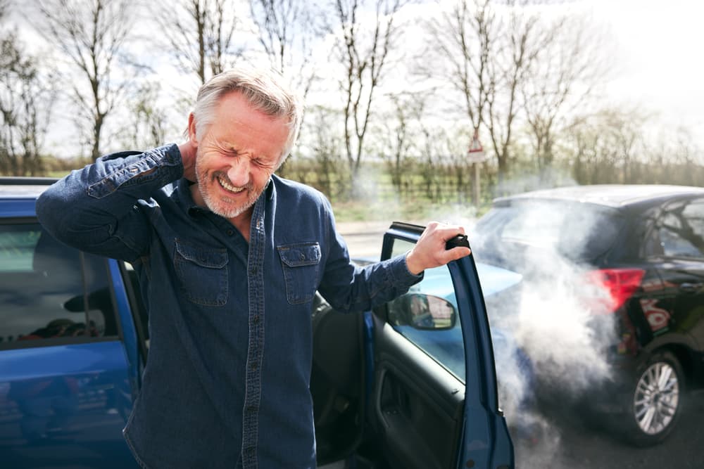 After a traffic accident, an elderly male driver, experiencing whiplash, steps out of the car, visibly in neck pain in Philadelphia, PA