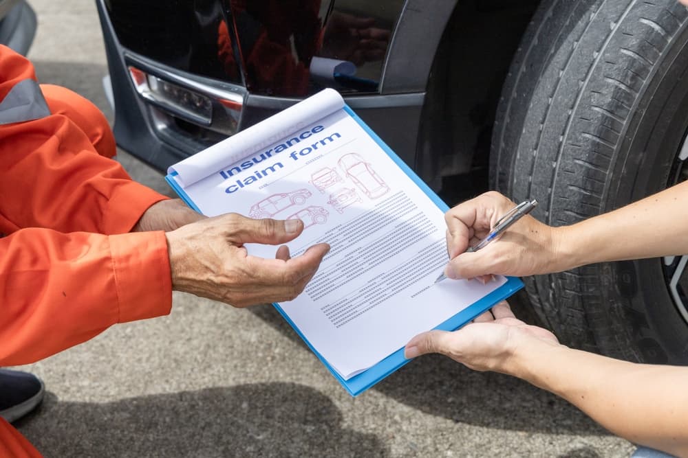 Insurance agent inspects road accident, assesses car damage, and customer signs claim form.