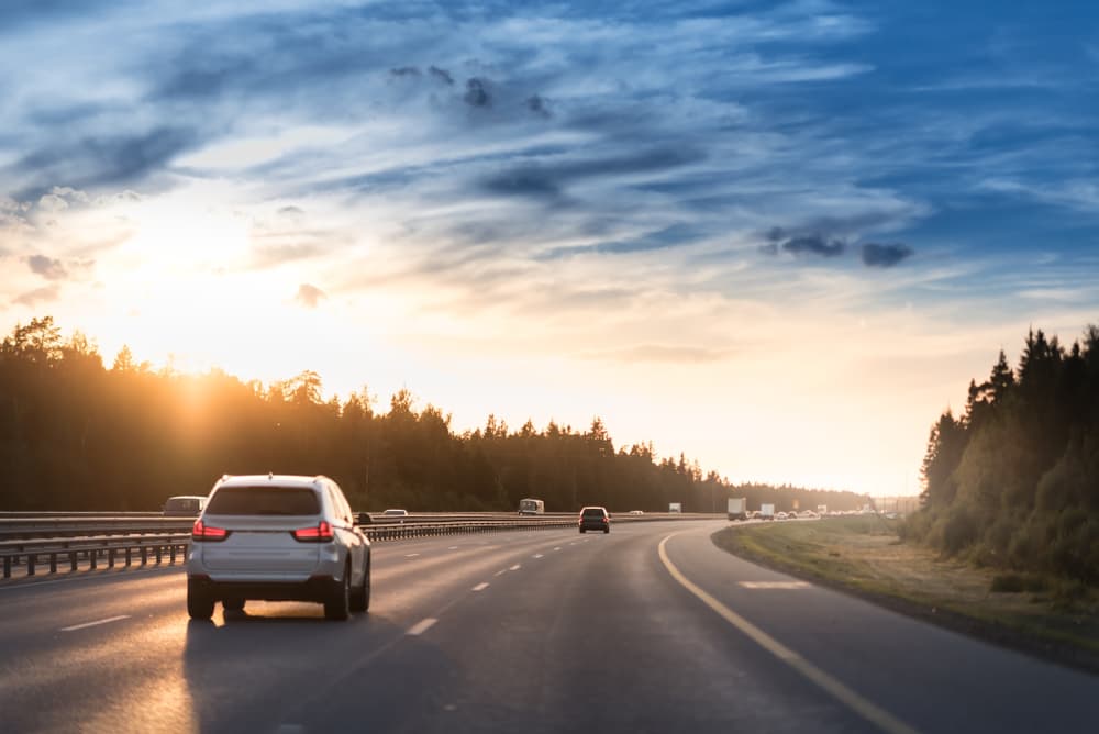 Experience the serene beauty of highway traffic at sunset, framed by metal safety barriers or rail, with cars gliding on asphalt under a dramatic cloudy sky.