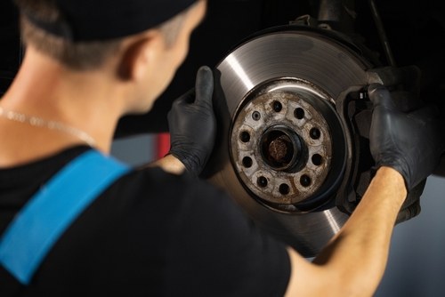 Mechanic in a workshop wearing gloves, carefully inspecting a car's disc brake during maintenance.