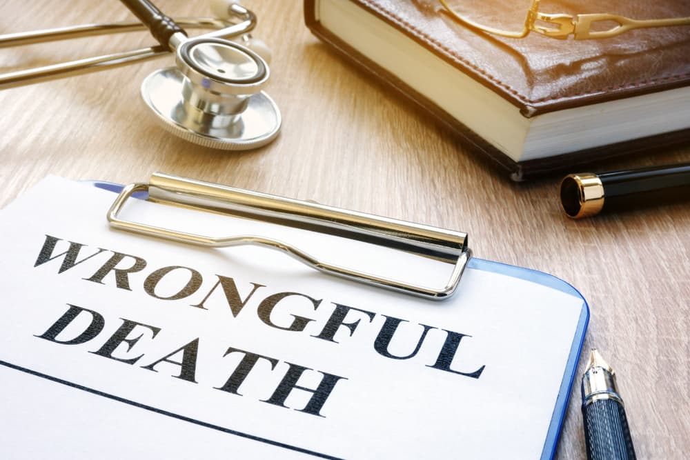 A clipboard with a "Wrongful Death" document, stethoscope, notebook, pen, and glasses on a desk.